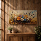 Panoramic painting depicting a vibrant cluster of wildflowers growing through tall meadow grasses. Bright blossoms in orange, blue, purple, and white rise from textured golden stems while loose expressive brushstrokes create movement across the floral arrangement and surrounding field.