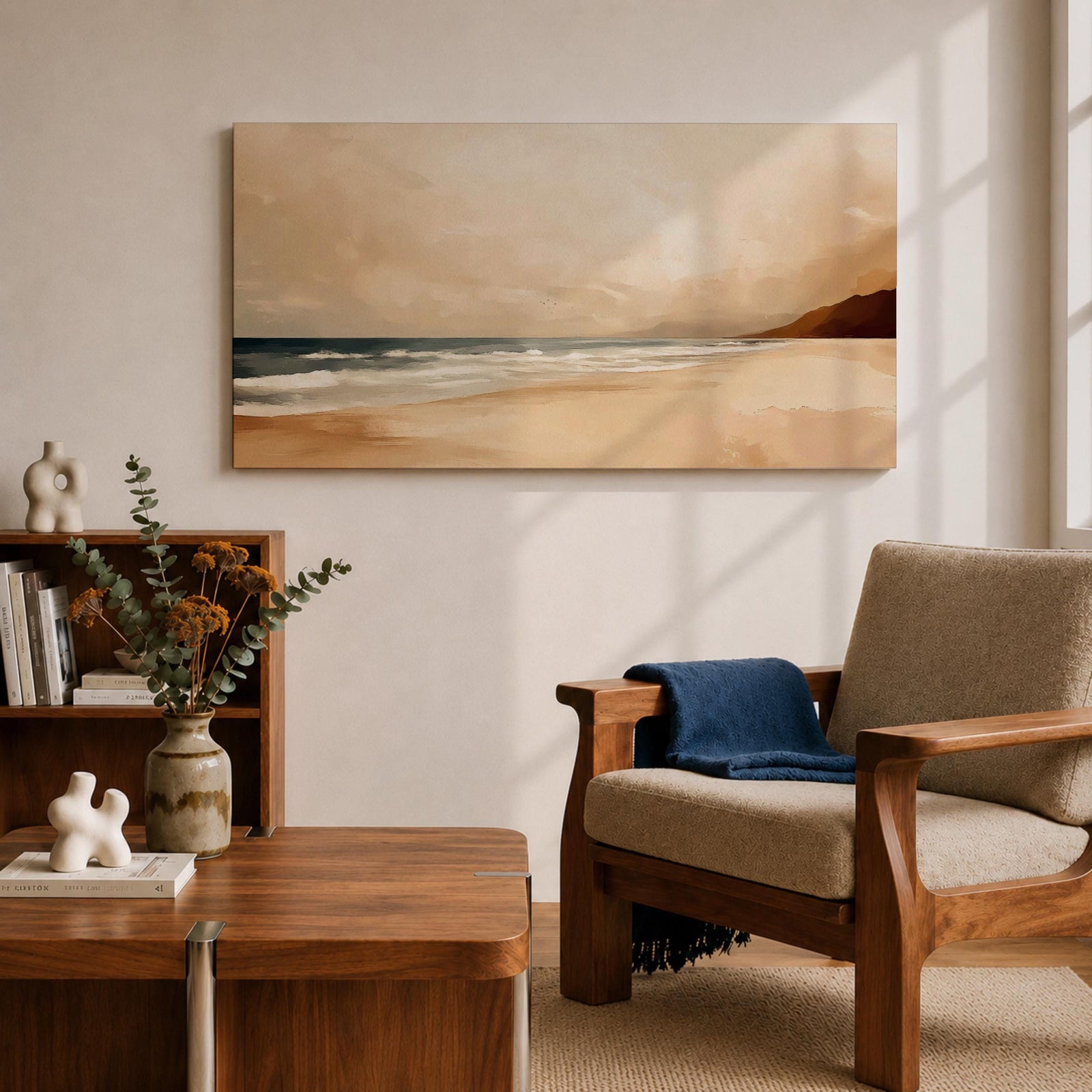 Panoramic coastal landscape painting showing a quiet sandy beach with gentle ocean waves rolling onto the shore beneath a soft sky. Subtle tones of beige, blue, and warm gray create a calm atmosphere while distant hills stretch along the horizon and light reflects across the water.