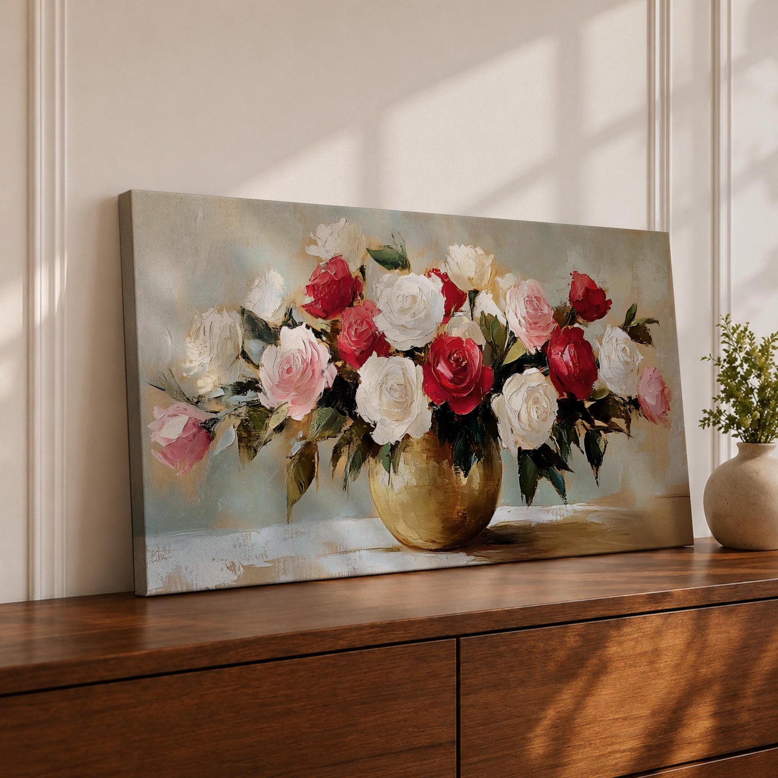 A panoramic still life painting of a large bouquet of red, white, and blush pink roses arranged in a round gold vase with green leaves spreading outward, rendered with textured brushstrokes and soft neutral background tones that emphasize the layered petals and balanced floral composition.