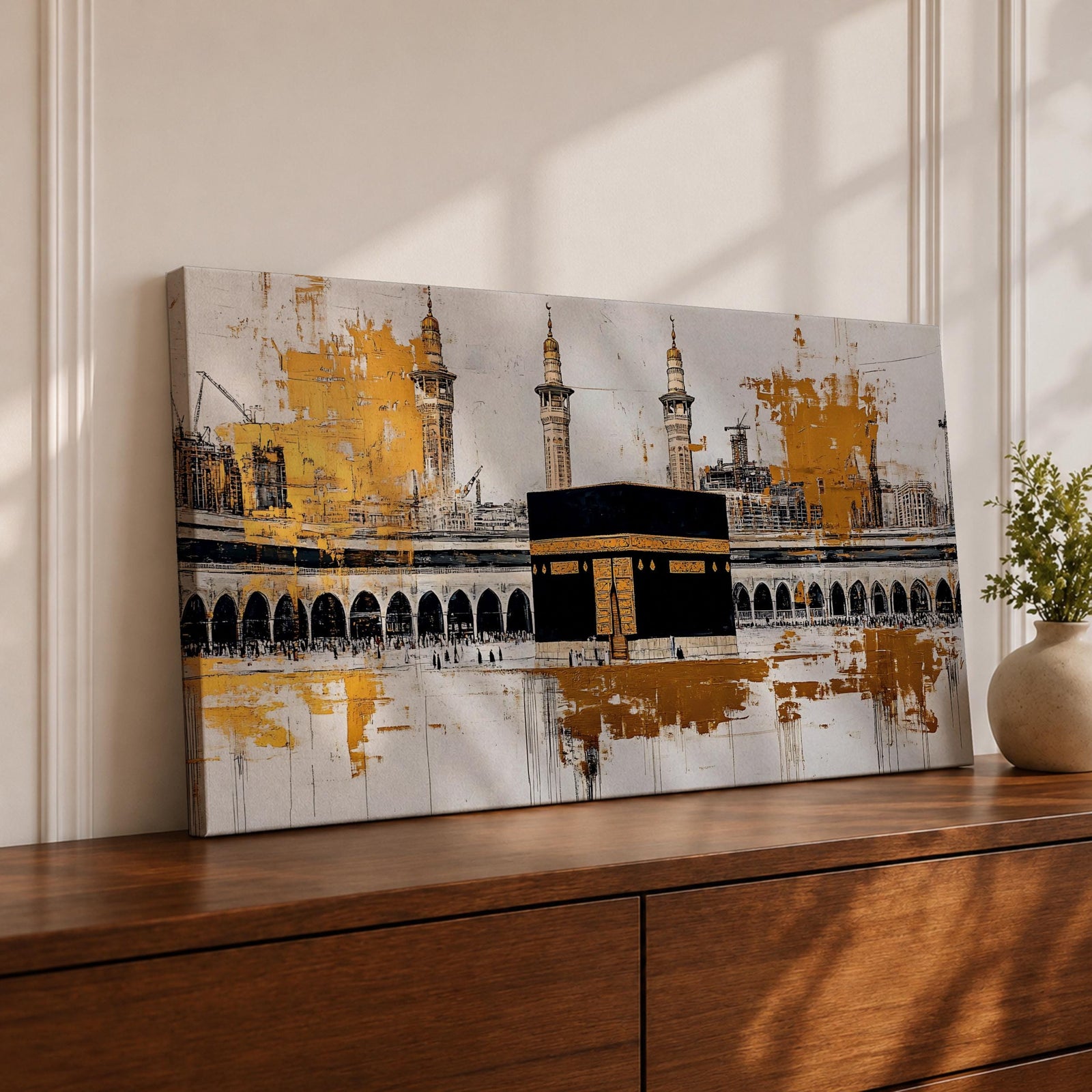 Panoramic painting of the Kaaba in Mecca centered within Masjid al Haram featuring the black cube sanctuary draped in the kiswah with gold calligraphy bands. Tall mosque minarets and long arched colonnades frame the courtyard while bold gold abstract paint textures and layered architectural lines extend across the wide horizontal composition.