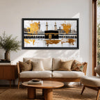 Panoramic painting of the Kaaba in Mecca centered within Masjid al Haram featuring the black cube sanctuary draped in the kiswah with gold calligraphy bands. Tall mosque minarets and long arched colonnades frame the courtyard while bold gold abstract paint textures and layered architectural lines extend across the wide horizontal composition.