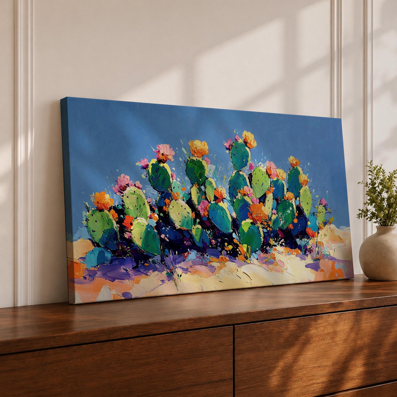 Panoramic painting of desert prickly pear cactus plants with bright pink and yellow blooming flowers growing across a colorful arid landscape. Thick palette knife brushstrokes create textured cactus pads vibrant blossoms and layered desert hills beneath a glowing sky forming a wide southwestern desert scene.