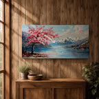 Panoramic painting of a cherry blossom tree in full bloom beside a calm mountain lake with snow covered peaks in the distance and soft clouds above. Pink petals drift across the water while thick palette knife brushstrokes create texture in the blossoms shoreline and reflections forming a wide spring landscape scene with bold color contrast.