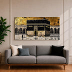 Panoramic gold and black painting of the Kaaba at Masjid al Haram in Mecca, showing the cubed sanctuary draped in the black kiswah with gold calligraphy bands. Surrounding mosque arches and marble courtyard stretch across the horizontal composition while small pilgrim figures circle the Kaaba creating scale and depth.