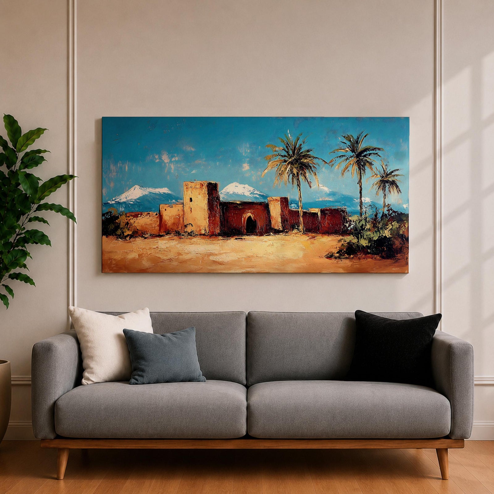 Panoramic painting of a Moroccan kasbah built from warm earthen walls set in a desert landscape with tall palm trees and distant snow capped mountains beneath a bright blue sky. Thick palette knife textures shape the fortress architecture sandy ground and foliage creating a wide horizontal North African landscape scene with bold contrast.