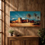 Panoramic painting of a Moroccan kasbah built from warm earthen walls set in a desert landscape with tall palm trees and distant snow capped mountains beneath a bright blue sky. Thick palette knife textures shape the fortress architecture sandy ground and foliage creating a wide horizontal North African landscape scene with bold contrast.