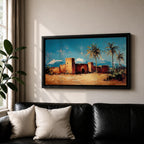 Panoramic painting of a Moroccan kasbah built from warm earthen walls set in a desert landscape with tall palm trees and distant snow capped mountains beneath a bright blue sky. Thick palette knife textures shape the fortress architecture sandy ground and foliage creating a wide horizontal North African landscape scene with bold contrast.