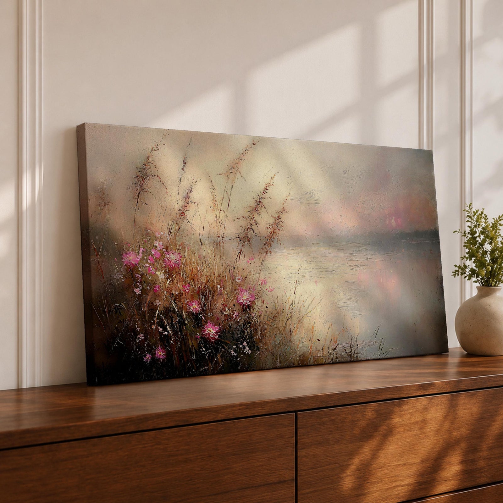 Panoramic landscape painting of soft pink wildflowers and tall grasses growing along a calm lakeshore. The scene features delicate meadow blooms in the foreground with textured brushstrokes and warm earthy tones, fading into a misty reflective lake and distant horizon under a gentle sky.