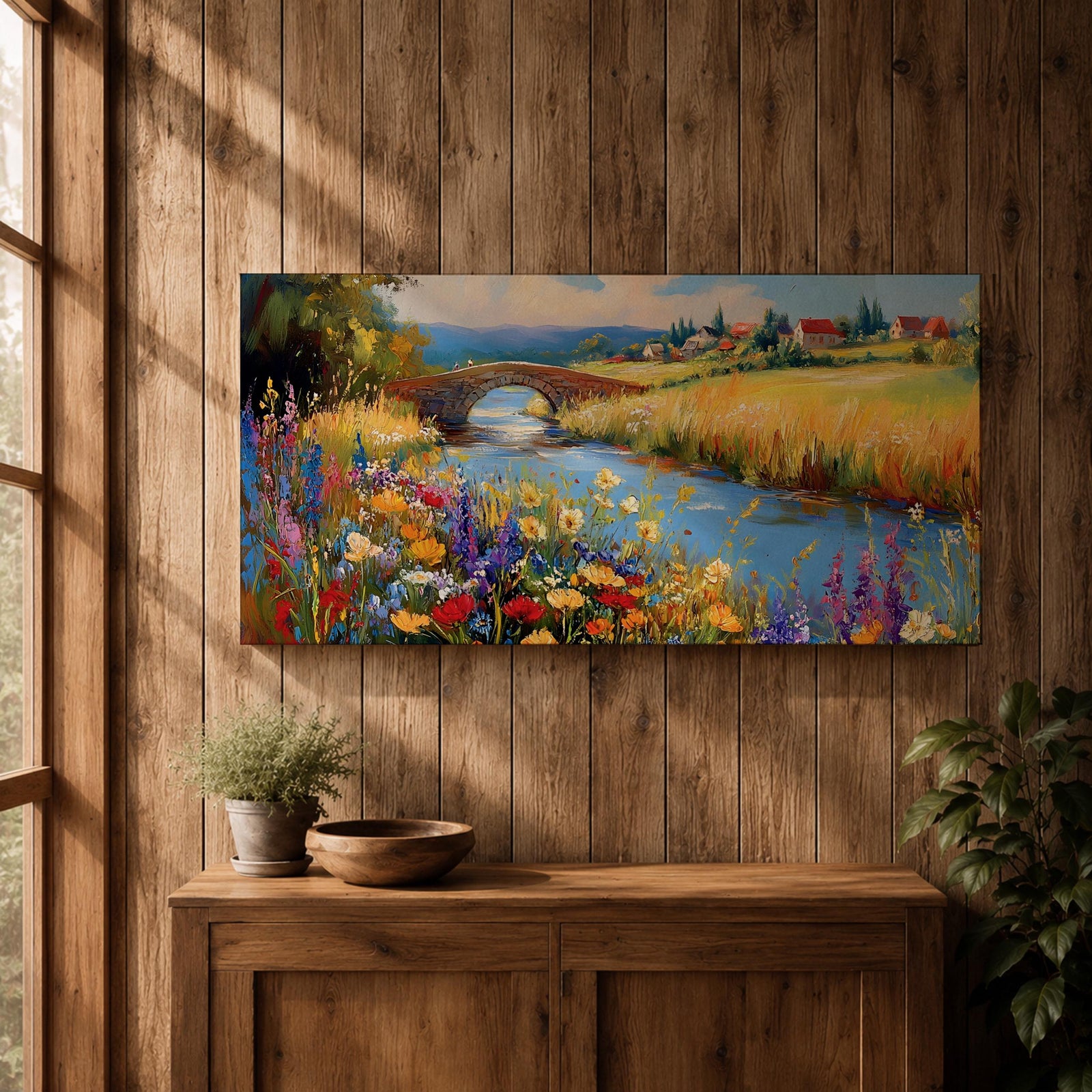 Panoramic landscape painting of a winding river flowing through a countryside meadow filled with colorful wildflowers. A small stone bridge arches over the water while fields, cottages, and rolling hills stretch into the distance under a bright sky, rendered with vibrant textured brushstrokes.