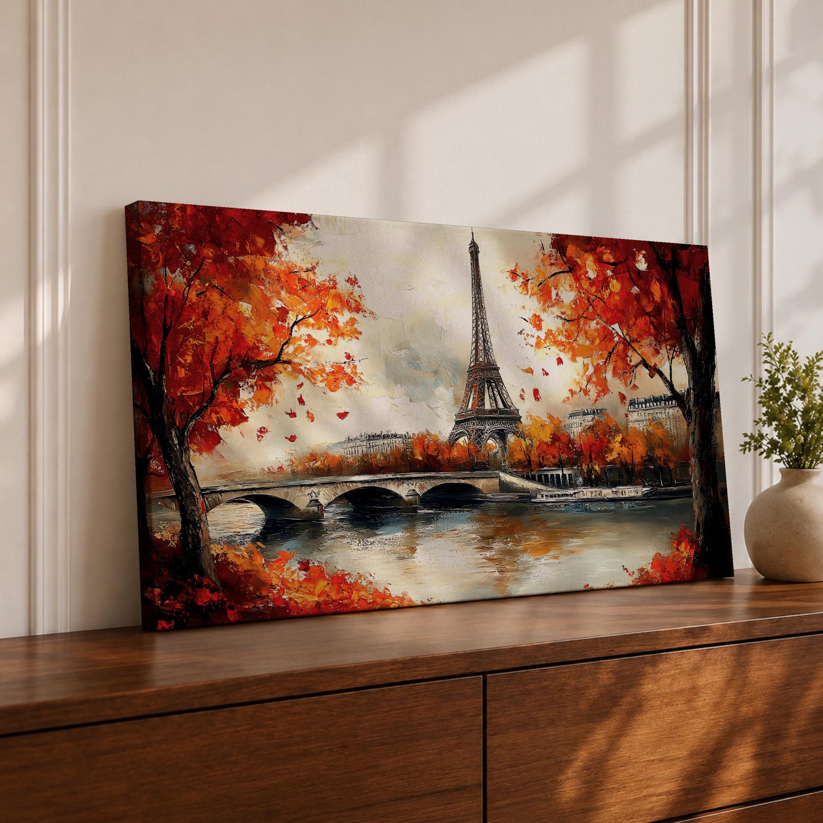 Panoramic painting of the Eiffel Tower rising above the Seine River with an arched stone bridge and classic Parisian buildings along the waterfront. Vibrant red and orange autumn trees frame the scene while textured brushstrokes reflect warm foliage and architecture across the calm river surface.
