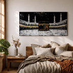 Panoramic artwork of the Kaaba at Masjid al-Haram in Mecca with black and gold accents surrounded by mosque arches and tall minarets against a dark night background.