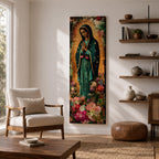 A tall narrow vertical painting of the Virgin Mary Guadalupe shown in prayer with hands clasped, wearing a deep teal mantle adorned with gold stars and a soft pink dress, surrounded by radiant golden rays, with rich floral elements in vibrant pink, red, and cream tones at the base, rendered in a textured painterly style with warm, aged tones.