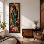 A tall narrow vertical painting of the Virgin Mary Guadalupe shown in prayer with hands clasped, wearing a deep teal mantle adorned with gold stars and a soft pink dress, surrounded by radiant golden rays, with rich floral elements in vibrant pink, red, and cream tones at the base, rendered in a textured painterly style with warm, aged tones.