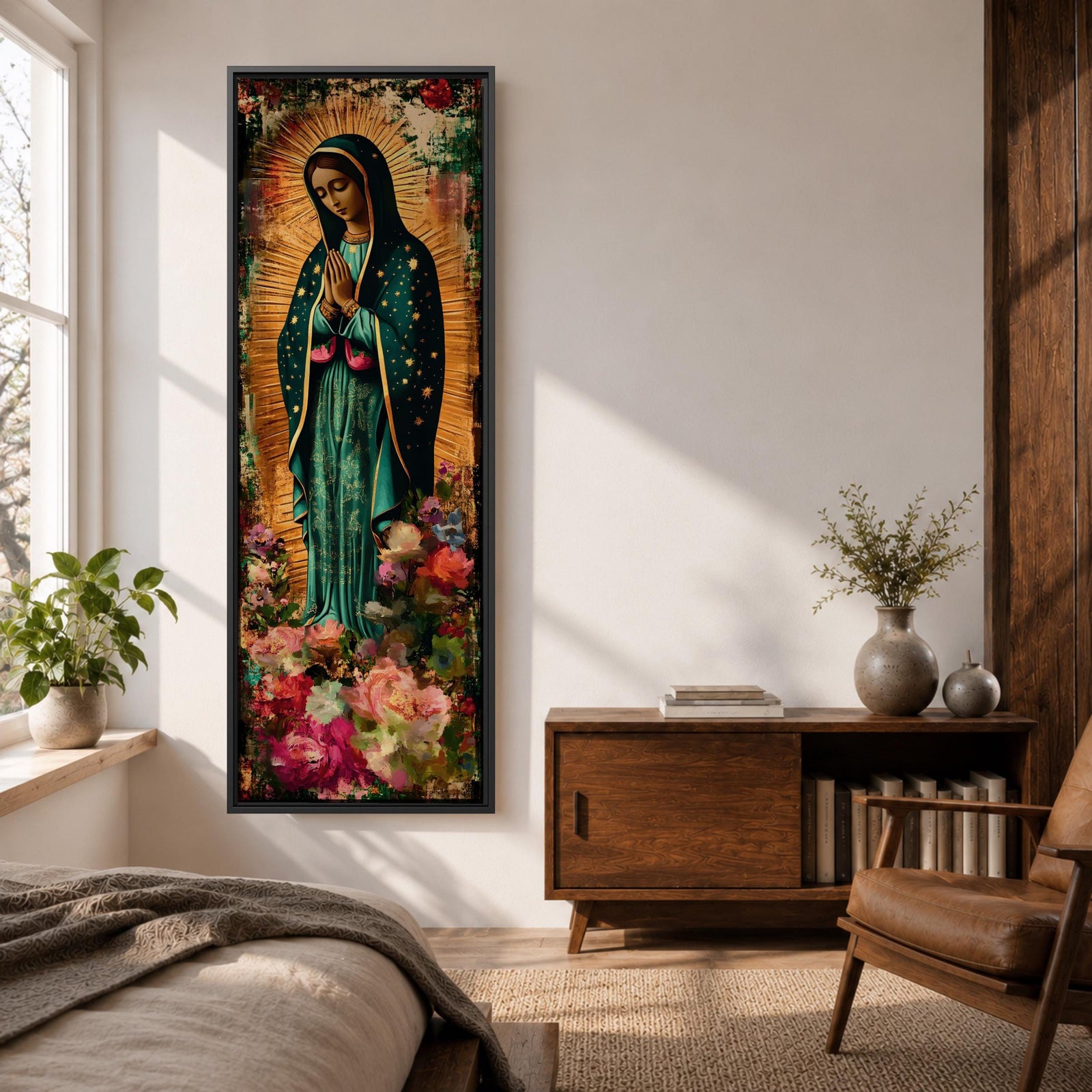 A tall narrow vertical painting of the Virgin Mary Guadalupe shown in prayer with hands clasped, wearing a deep teal mantle adorned with gold stars and a soft pink dress, surrounded by radiant golden rays, with rich floral elements in vibrant pink, red, and cream tones at the base, rendered in a textured painterly style with warm, aged tones.
