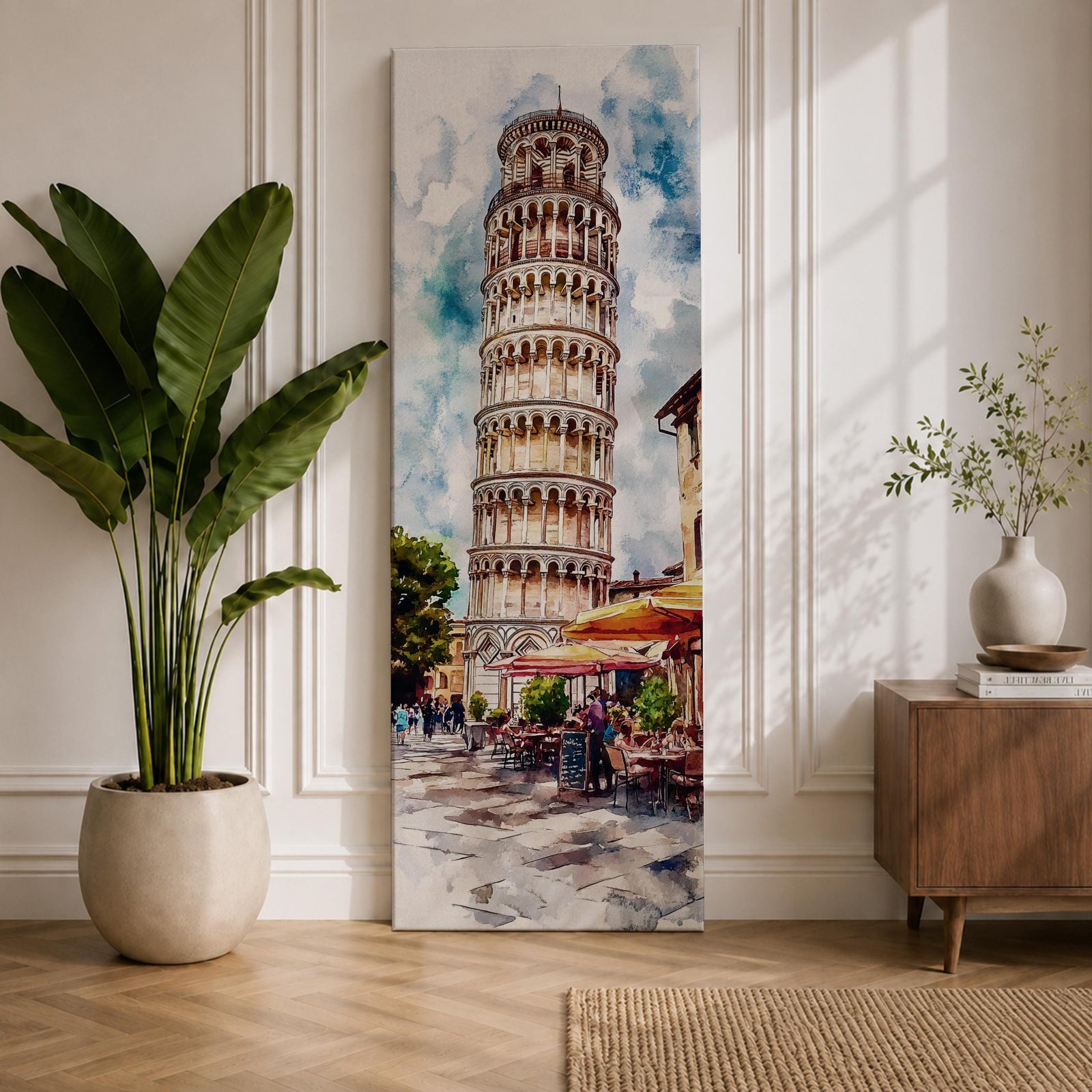 Long vertical watercolor style painting of the Leaning Tower rising above a lively Italian piazza with outdoor café tables and people walking along a stone street. The famous marble tower tilts gently against a bright sky while expressive brushstrokes capture the atmosphere of a historic Italian landmark and travel scene.