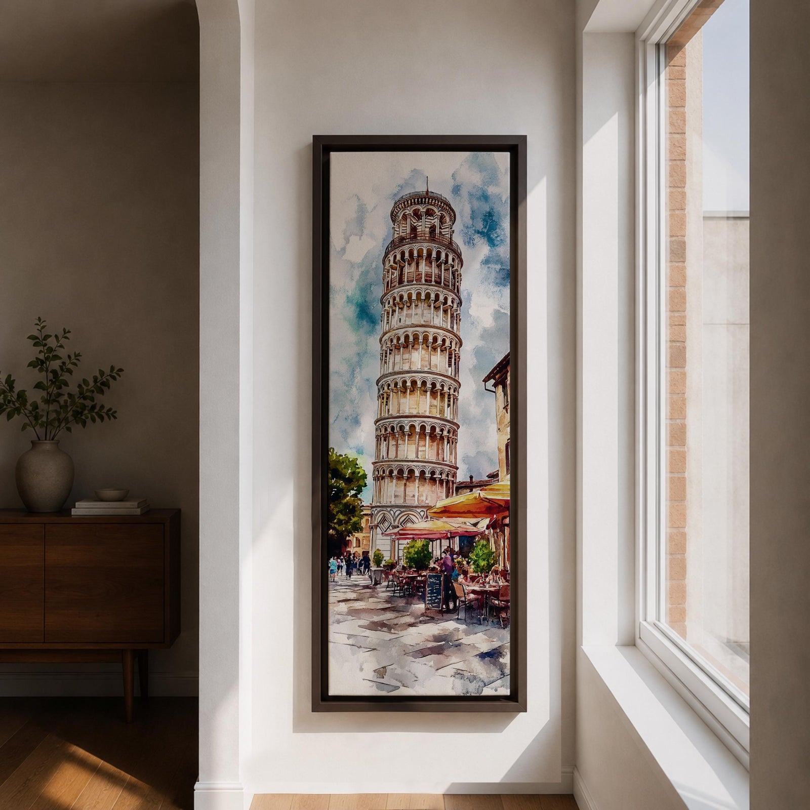 Long vertical watercolor style painting of the Leaning Tower rising above a lively Italian piazza with outdoor café tables and people walking along a stone street. The famous marble tower tilts gently against a bright sky while expressive brushstrokes capture the atmosphere of a historic Italian landmark and travel scene.