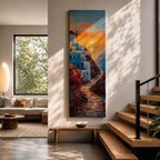A tall vertical painting depicts a Santorini coastal scene with whitewashed buildings perched along a cliffside, a winding stone path leading toward the sea, and a glowing sunset casting warm orange and gold light across the sky and water, with a windmill silhouette and small sailboats adding depth to the vibrant Mediterranean composition.