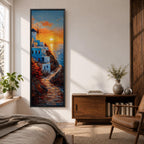 A tall vertical painting depicts a Santorini coastal scene with whitewashed buildings perched along a cliffside, a winding stone path leading toward the sea, and a glowing sunset casting warm orange and gold light across the sky and water, with a windmill silhouette and small sailboats adding depth to the vibrant Mediterranean composition.