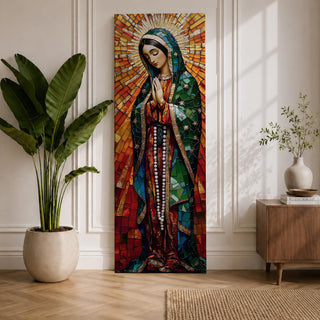 Long vertical stained glass style depiction of Our Lady of Guadalupe with hands clasped in prayer. She wears a green mantle decorated with stars and a red robe while radiant golden rays form a halo behind her, composed of colorful mosaic glass pieces forming a luminous devotional image.