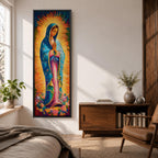 Long vertical painting of the Virgin Mary standing in prayer with hands together, wearing a blue mantle over a pink robe and surrounded by radiant golden rays. Colorful flowers gather at her feet while expressive brushstrokes and vibrant tones create a devotional depiction inspired by the Virgen de Guadalupe iconography.
