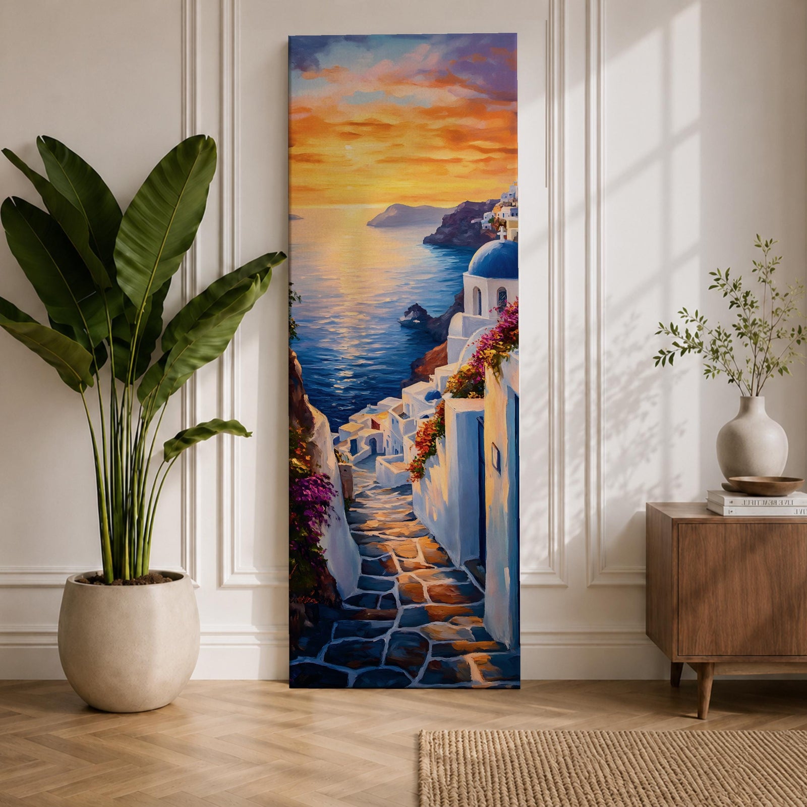 Long vertical painting of a Santorini coastal village with whitewashed buildings and a blue dome church overlooking the sea at sunset. A stone pathway descends between bright white walls toward the shoreline while golden sunlight reflects across calm water and warm clouds fill the sky.