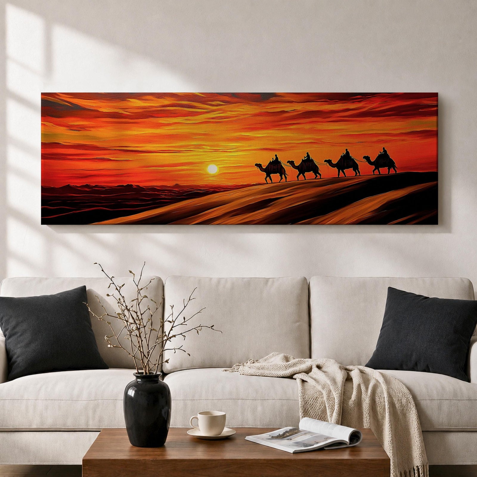 Panoramic desert sunset painting featuring a silhouette caravan of camels and riders walking along rolling sand dunes beneath a glowing red and orange sky. The low sun sits near the horizon while layered desert dunes stretch into the distance, creating a dramatic wide composition across the desert landscape.