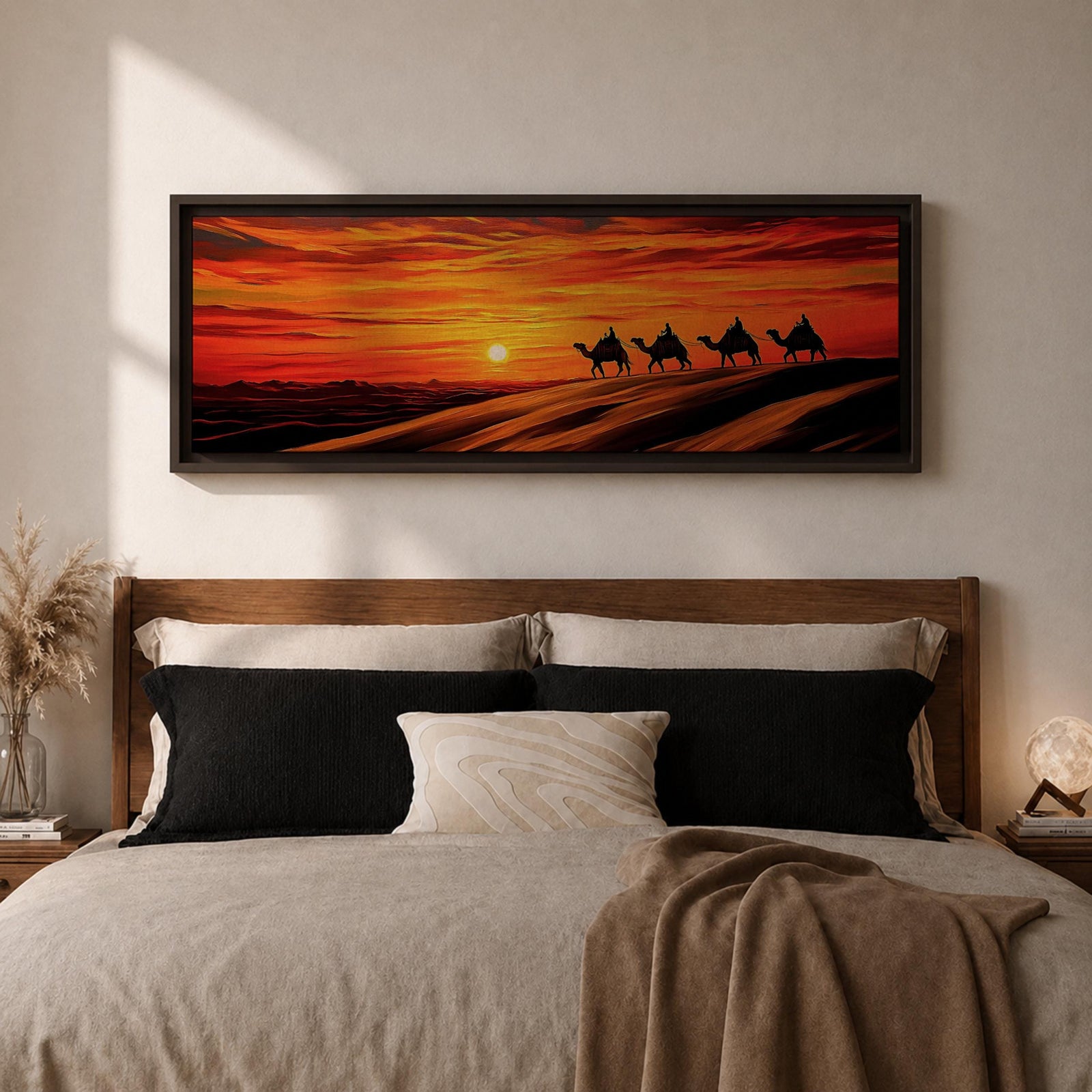 Panoramic desert sunset painting featuring a silhouette caravan of camels and riders walking along rolling sand dunes beneath a glowing red and orange sky. The low sun sits near the horizon while layered desert dunes stretch into the distance, creating a dramatic wide composition across the desert landscape.