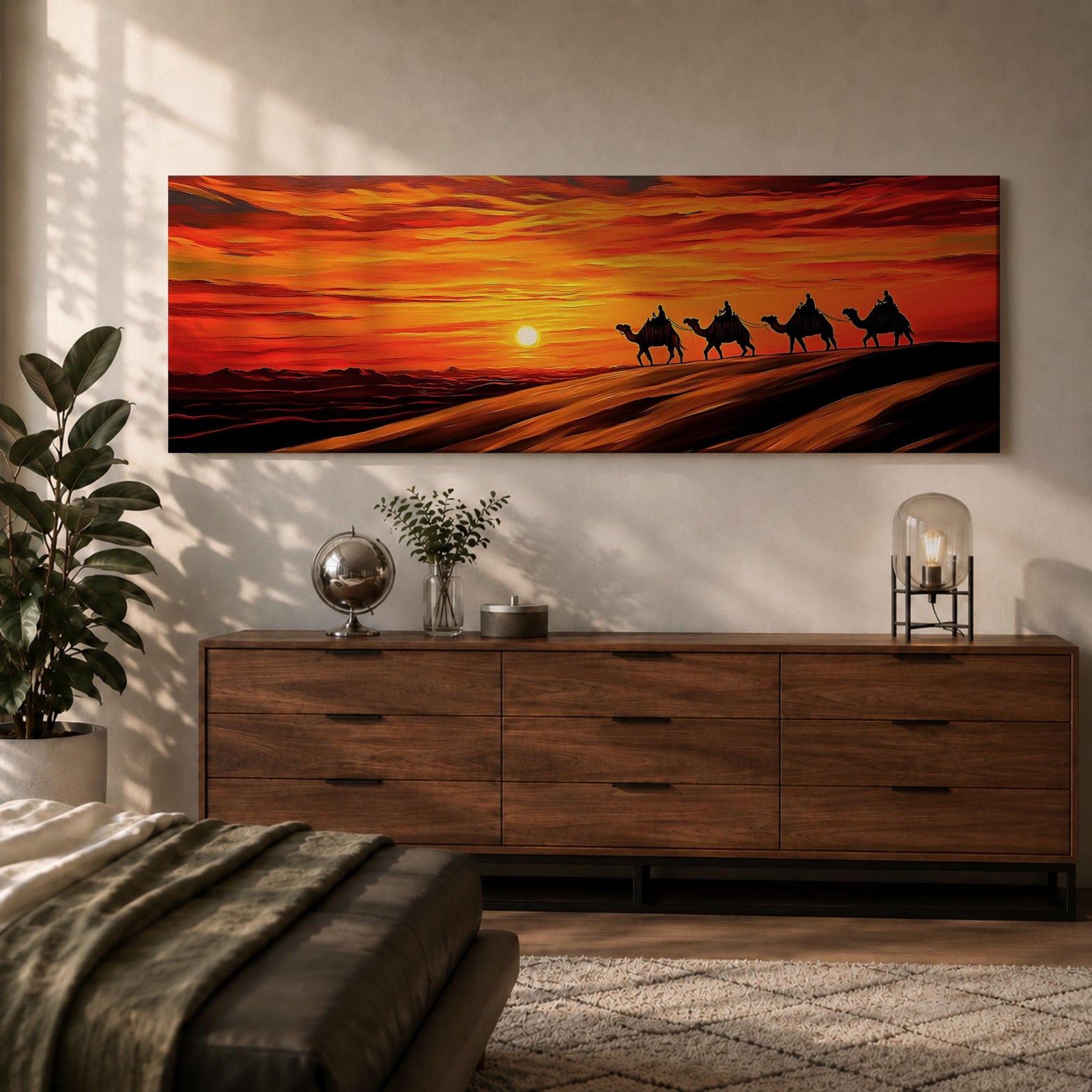 Panoramic desert sunset painting featuring a silhouette caravan of camels and riders walking along rolling sand dunes beneath a glowing red and orange sky. The low sun sits near the horizon while layered desert dunes stretch into the distance, creating a dramatic wide composition across the desert landscape.