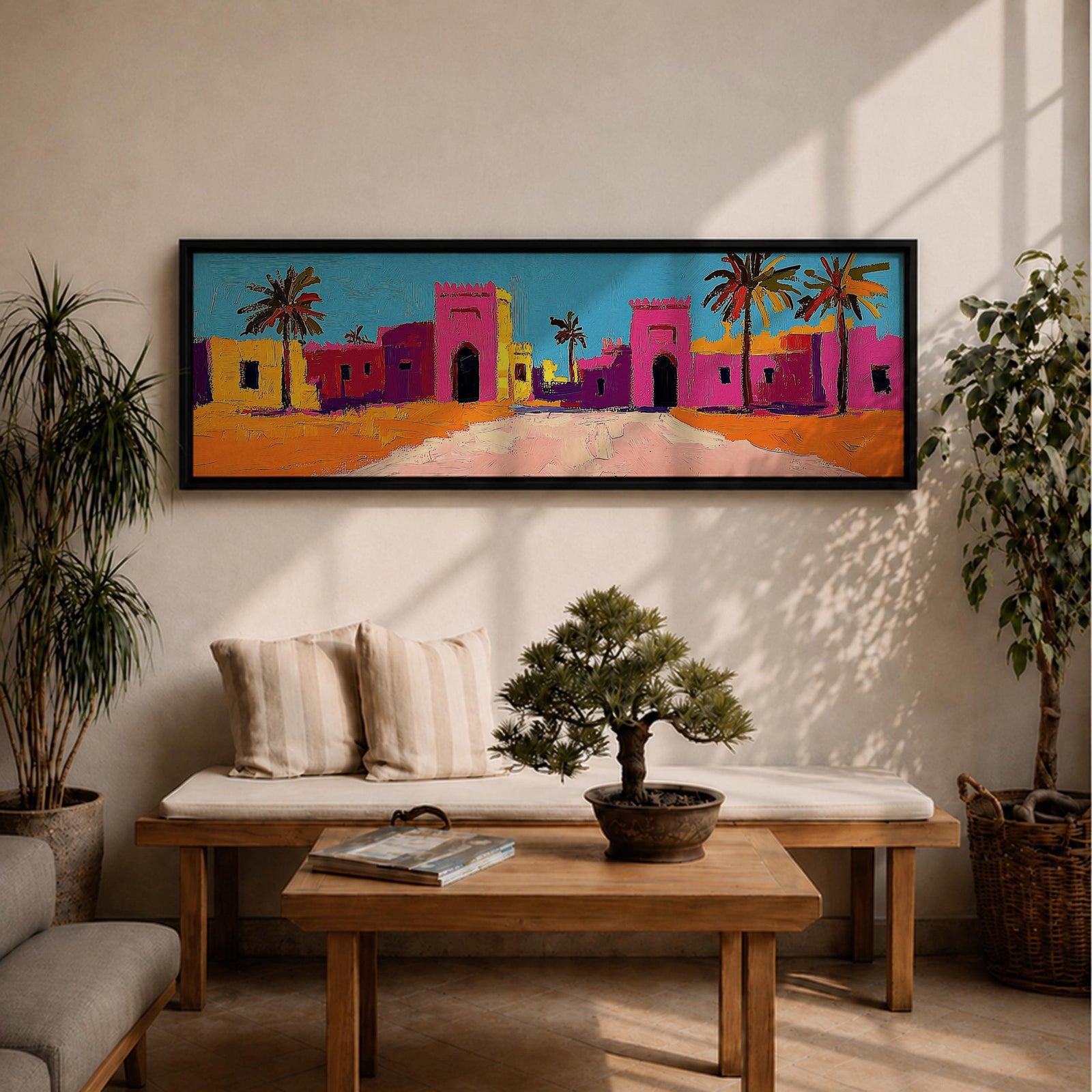 Panoramic desert village painting showing colorful Moroccan kasbah buildings in bright pink and warm ochre tones with tall palm trees lining a sandy road. Bold textured brushstrokes and vibrant colors create a lively North African scene beneath a clear blue sky across the wide horizontal composition.