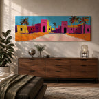 Panoramic desert village painting showing colorful Moroccan kasbah buildings in bright pink and warm ochre tones with tall palm trees lining a sandy road. Bold textured brushstrokes and vibrant colors create a lively North African scene beneath a clear blue sky across the wide horizontal composition.