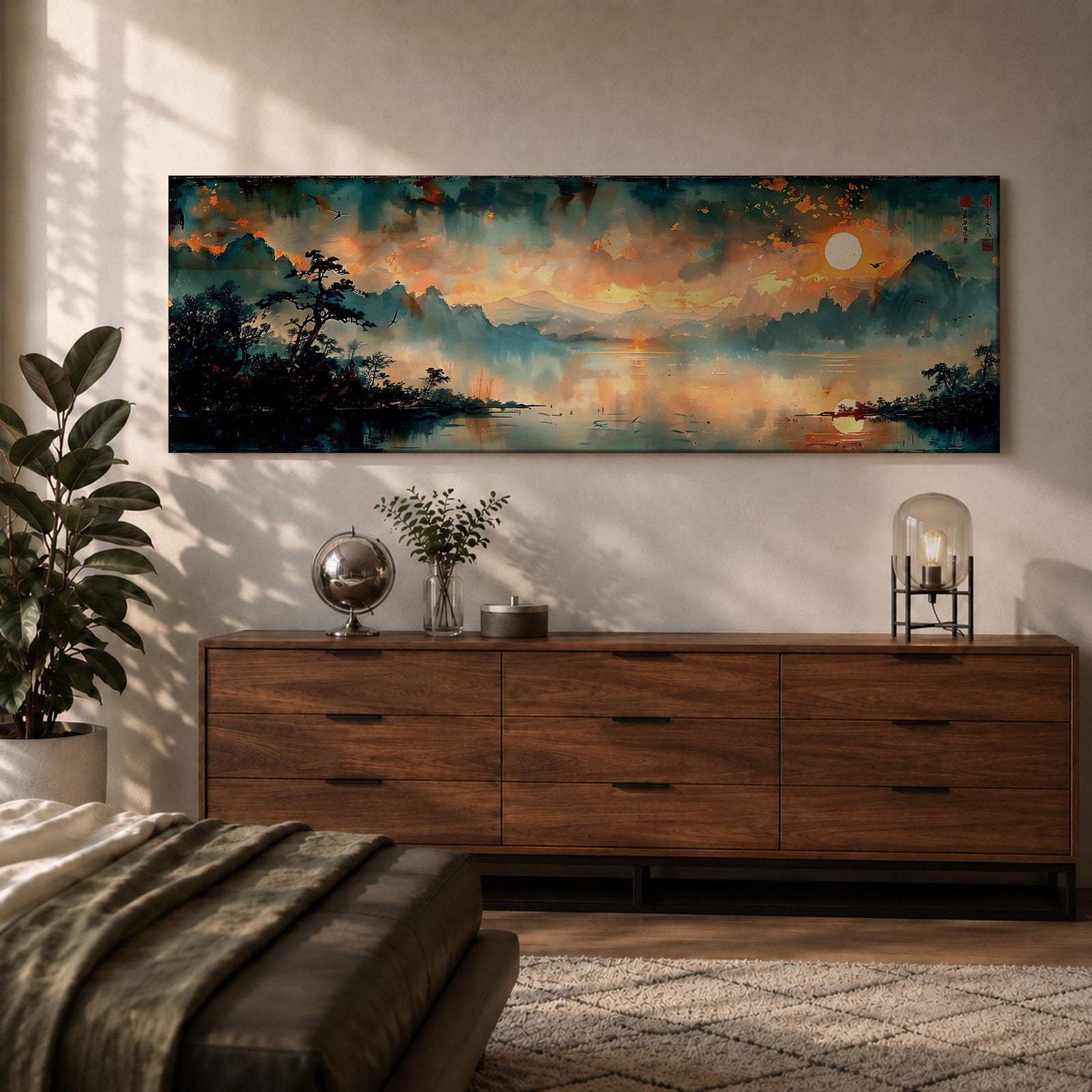 Panoramic Chinese landscape painting of misty mountains rising above a tranquil lake at sunset with warm orange light reflecting across the water. Dark tree silhouettes frame the shoreline while distant peaks fade into atmospheric haze beneath dramatic clouds in a traditional oriental scenery composition.
