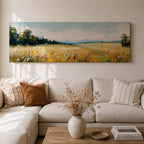 Panoramic countryside landscape painting showing a wide golden field filled with tall grasses and scattered wildflowers. A tree line borders the meadow while distant hills stretch across the horizon beneath a soft blue sky with light clouds across the expansive rural scene.
