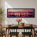 Panoramic artwork showing a flock of flamingos standing in shallow reflective water at sunset. The long horizontal composition features pink birds mirrored in the calm lake surface with glowing orange, purple, and magenta sky tones behind them, creating a tropical waterscape with silhouettes and soft reflections stretching across the scene.