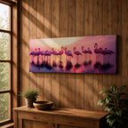 Panoramic artwork showing a flock of flamingos standing in shallow reflective water at sunset. The long horizontal composition features pink birds mirrored in the calm lake surface with glowing orange, purple, and magenta sky tones behind them, creating a tropical waterscape with silhouettes and soft reflections stretching across the scene.