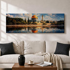 Panoramic canvas artwork depicting the Dome of the Rock in Jerusalem with its iconic golden dome and blue tiled octagonal structure rising above surrounding trees and historic buildings, reflected in calm water in the foreground beneath a bright sky filled with scattered clouds, rendered in a detailed landscape style emphasizing the architecture and skyline of the sacred site.