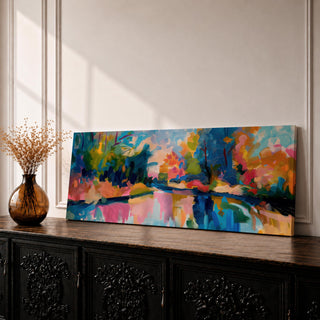 Panoramic abstract landscape painting featuring expressive brushstrokes and vivid colors portraying trees and foliage surrounding a calm reflective river, with bright tones of blue, pink, orange, green, and yellow blending across sky and water to create a contemporary impressionistic nature scene with dynamic movement and layered texture.