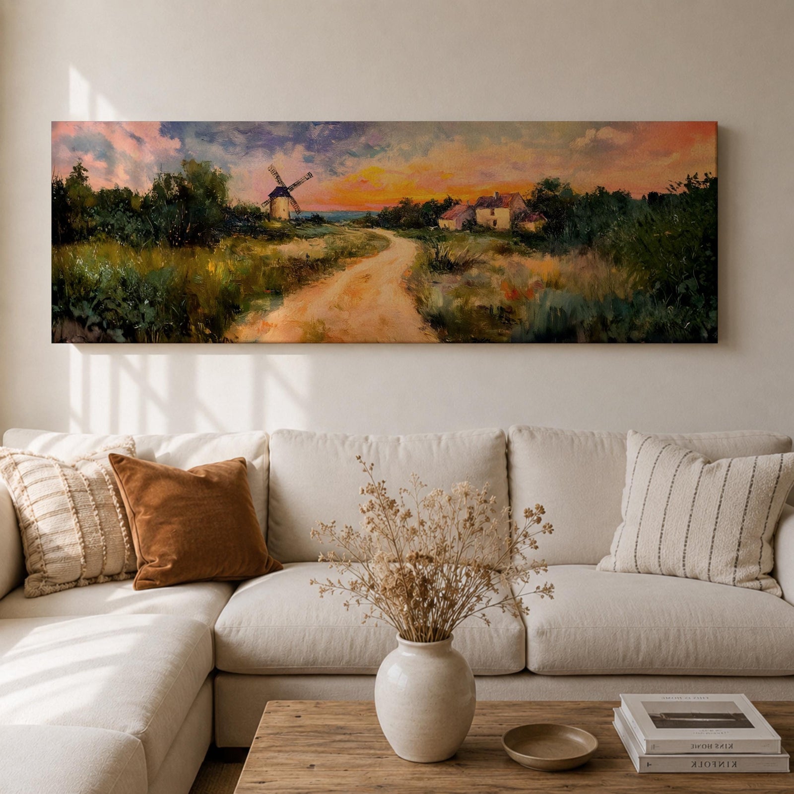 A panoramic countryside landscape painting showing a winding dirt road leading through grassy fields toward a traditional windmill and small farmhouse under a glowing sunset sky, with soft clouds and warm golden light illuminating the rural scenery across the wide composition.