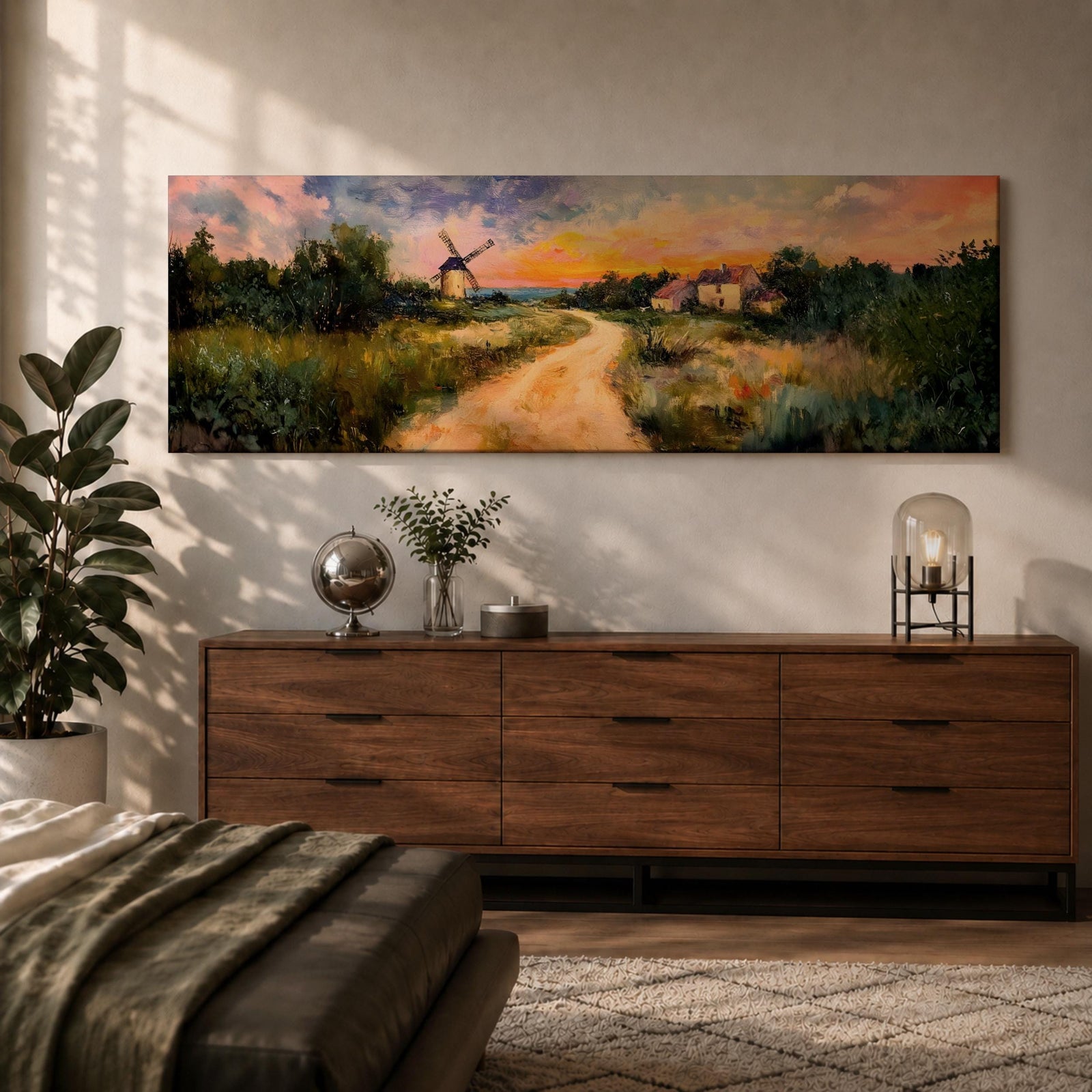 A panoramic countryside landscape painting showing a winding dirt road leading through grassy fields toward a traditional windmill and small farmhouse under a glowing sunset sky, with soft clouds and warm golden light illuminating the rural scenery across the wide composition.