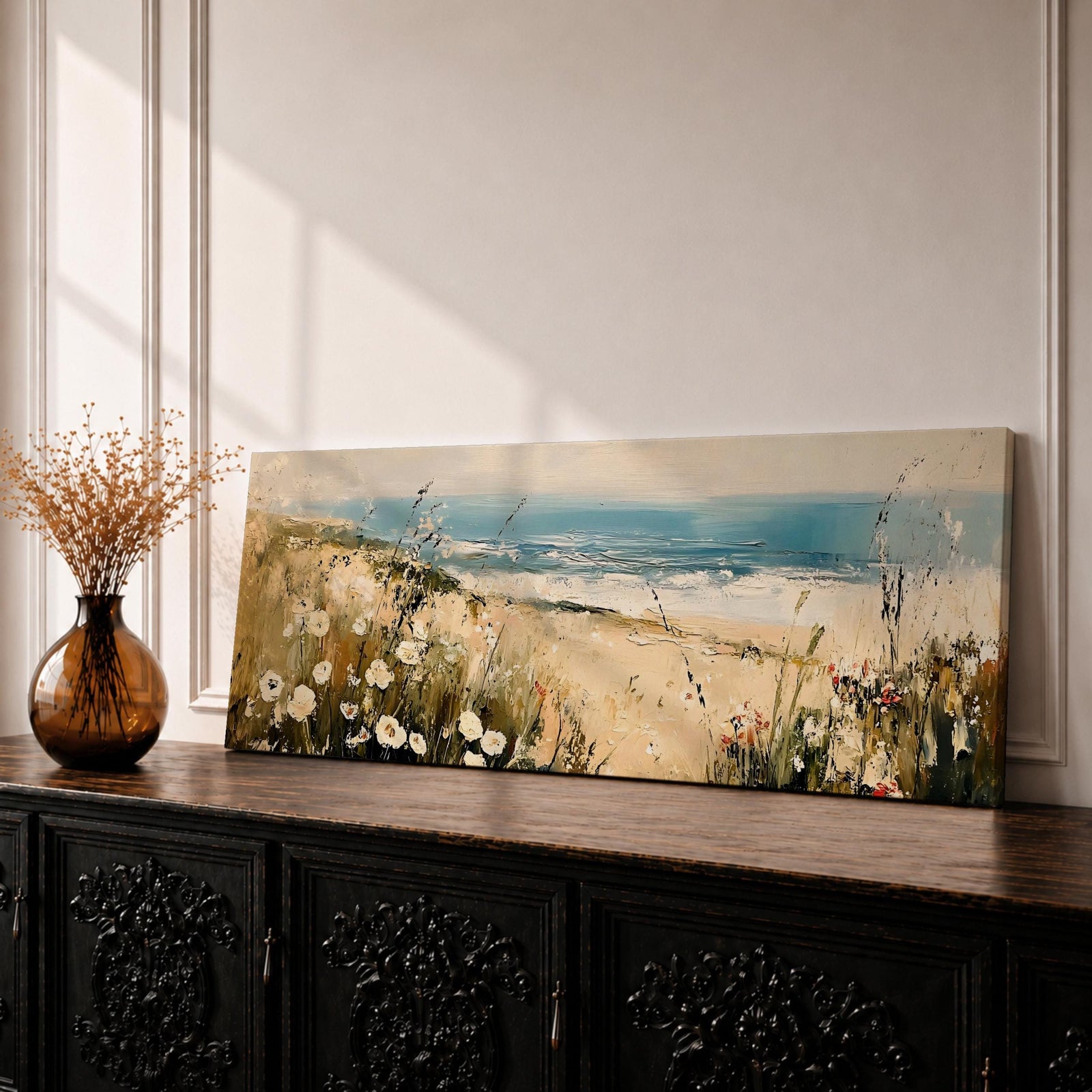 A long panoramic coastal painting showing sandy dunes covered with wild grasses and small white flowers overlooking a calm ocean shoreline. Soft waves roll toward the beach beneath a pale blue sky while textured brush strokes create a peaceful seascape landscape stretching across a wide horizontal composition.