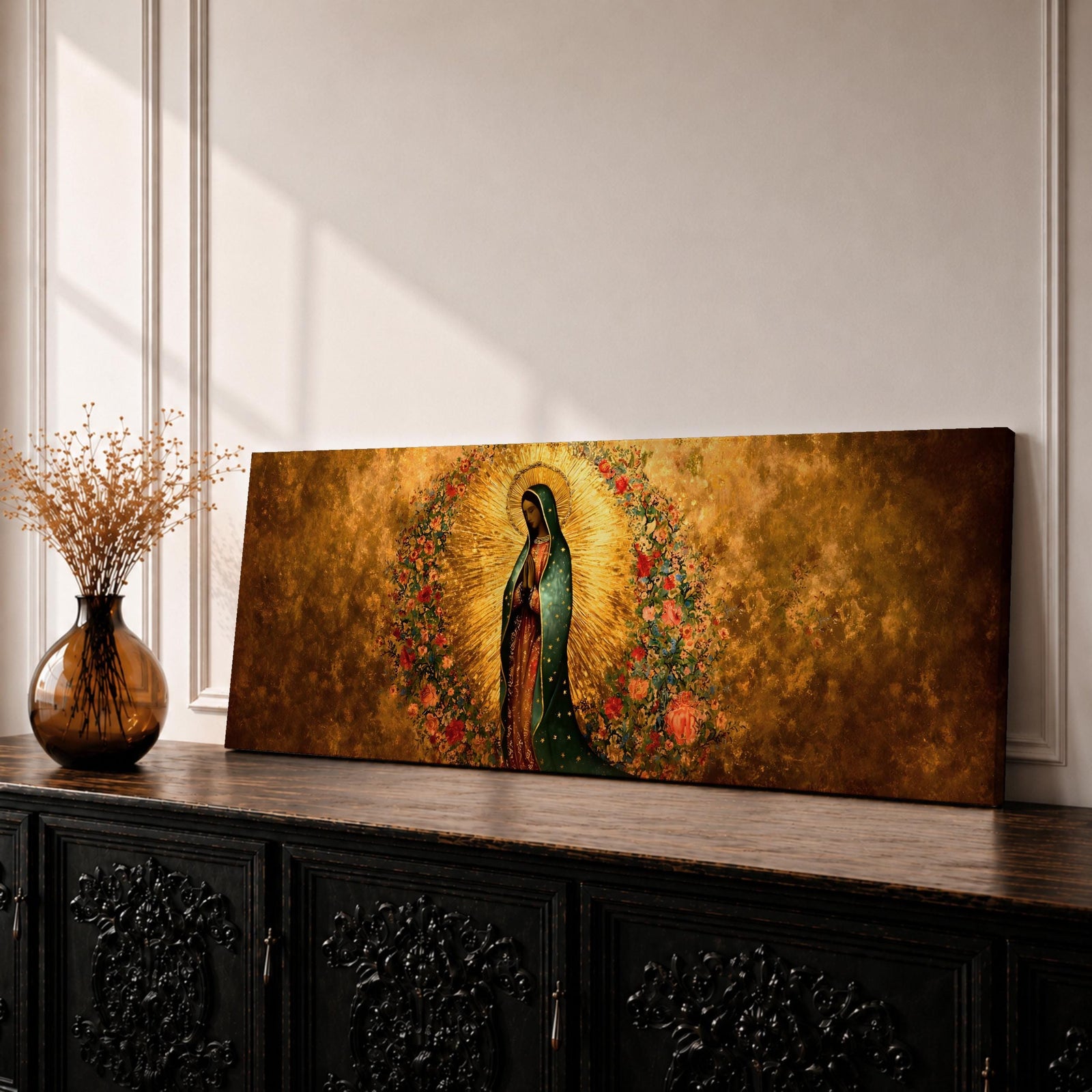 A long panoramic artwork depicting Our Lady of Guadalupe standing in prayer with folded hands and bowed head. She wears a green star covered mantle over a rose colored gown and is surrounded by radiant golden rays and a wreath of vibrant flowers, forming a traditional Catholic Marian image in a wide horizontal composition.