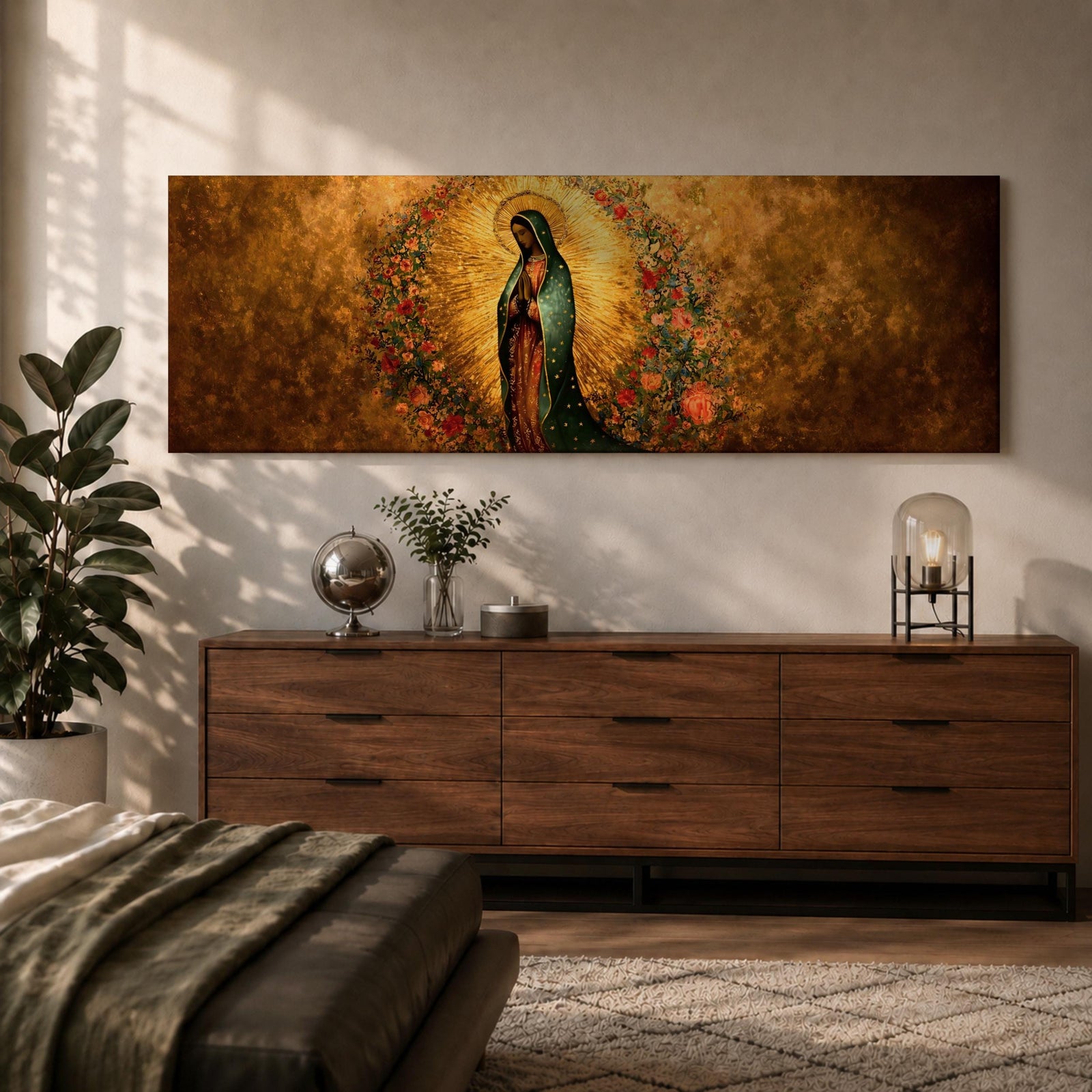 A long panoramic artwork depicting Our Lady of Guadalupe standing in prayer with folded hands and bowed head. She wears a green star covered mantle over a rose colored gown and is surrounded by radiant golden rays and a wreath of vibrant flowers, forming a traditional Catholic Marian image in a wide horizontal composition.