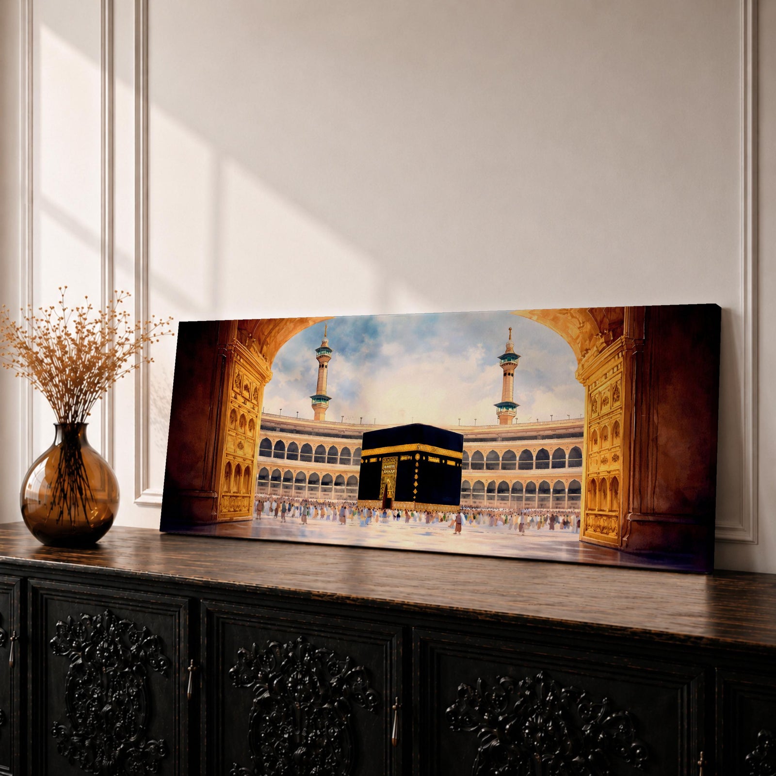 A long panoramic artwork depicting the Kaaba at the center of Masjid Al Haram in Mecca framed by grand mosque arches and tall minarets. The sacred black cube stands in the courtyard while pilgrims gather around it, creating a wide horizontal composition highlighting the holy Islamic sanctuary.