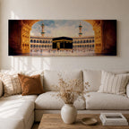 A long panoramic artwork depicting the Kaaba at the center of Masjid Al Haram in Mecca framed by grand mosque arches and tall minarets. The sacred black cube stands in the courtyard while pilgrims gather around it, creating a wide horizontal composition highlighting the holy Islamic sanctuary.