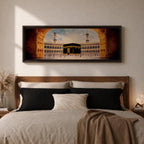 A long panoramic artwork depicting the Kaaba at the center of Masjid Al Haram in Mecca framed by grand mosque arches and tall minarets. The sacred black cube stands in the courtyard while pilgrims gather around it, creating a wide horizontal composition highlighting the holy Islamic sanctuary.