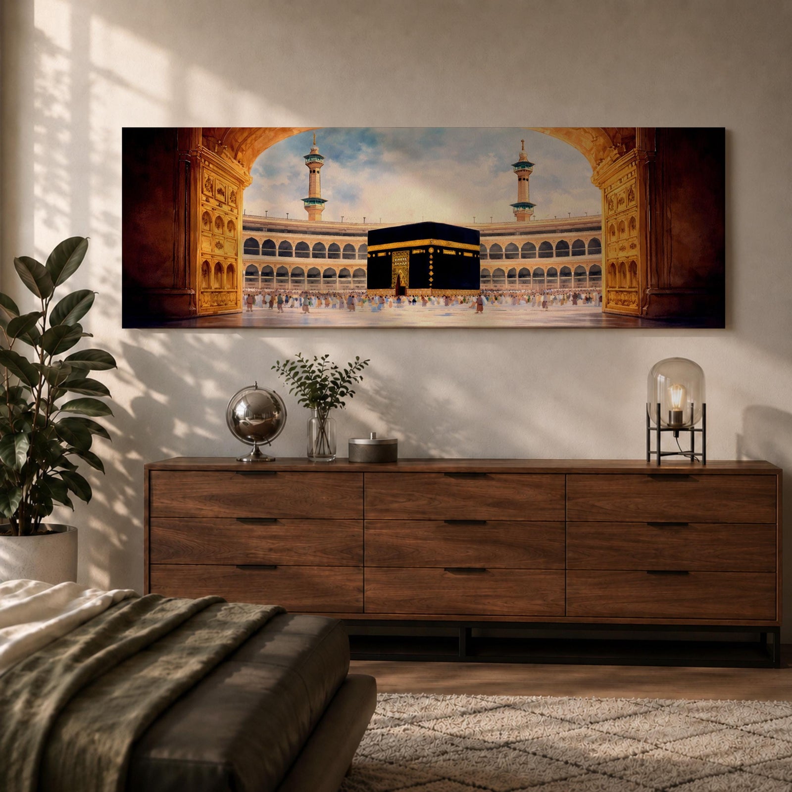 A long panoramic artwork depicting the Kaaba at the center of Masjid Al Haram in Mecca framed by grand mosque arches and tall minarets. The sacred black cube stands in the courtyard while pilgrims gather around it, creating a wide horizontal composition highlighting the holy Islamic sanctuary.
