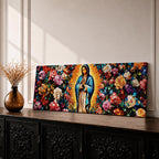 A long panoramic painting of Mary of Guadalupe standing in prayer with hands folded and head bowed, surrounded by radiant golden rays. She wears a blue mantle over a rose colored gown while vibrant roses and colorful flowers fill the background, creating a devotional Catholic Marian image across a wide horizontal composition.
