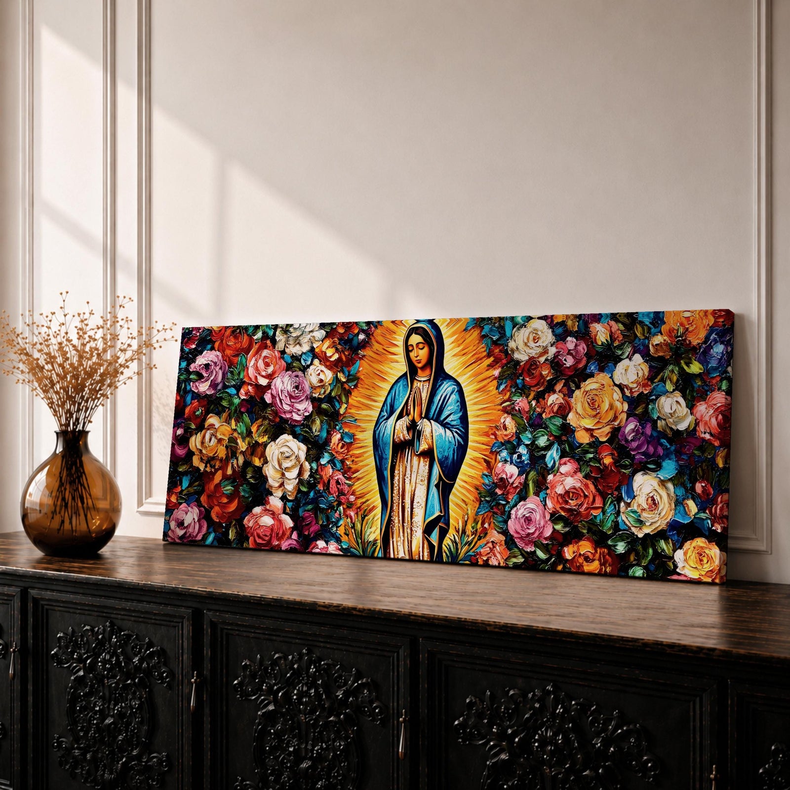 A long panoramic painting of Mary of Guadalupe standing in prayer with hands folded and head bowed, surrounded by radiant golden rays. She wears a blue mantle over a rose colored gown while vibrant roses and colorful flowers fill the background, creating a devotional Catholic Marian image across a wide horizontal composition.