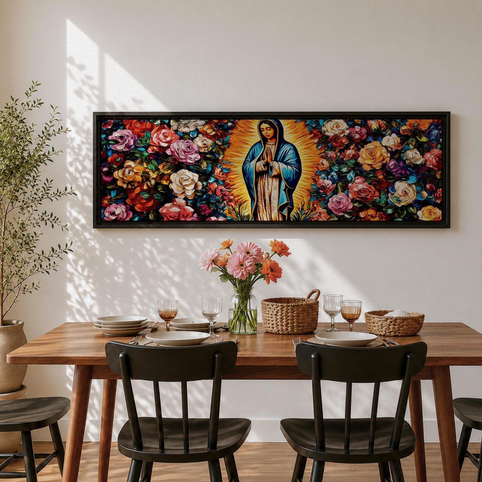 A long panoramic painting of Mary of Guadalupe standing in prayer with hands folded and head bowed, surrounded by radiant golden rays. She wears a blue mantle over a rose colored gown while vibrant roses and colorful flowers fill the background, creating a devotional Catholic Marian image across a wide horizontal composition.