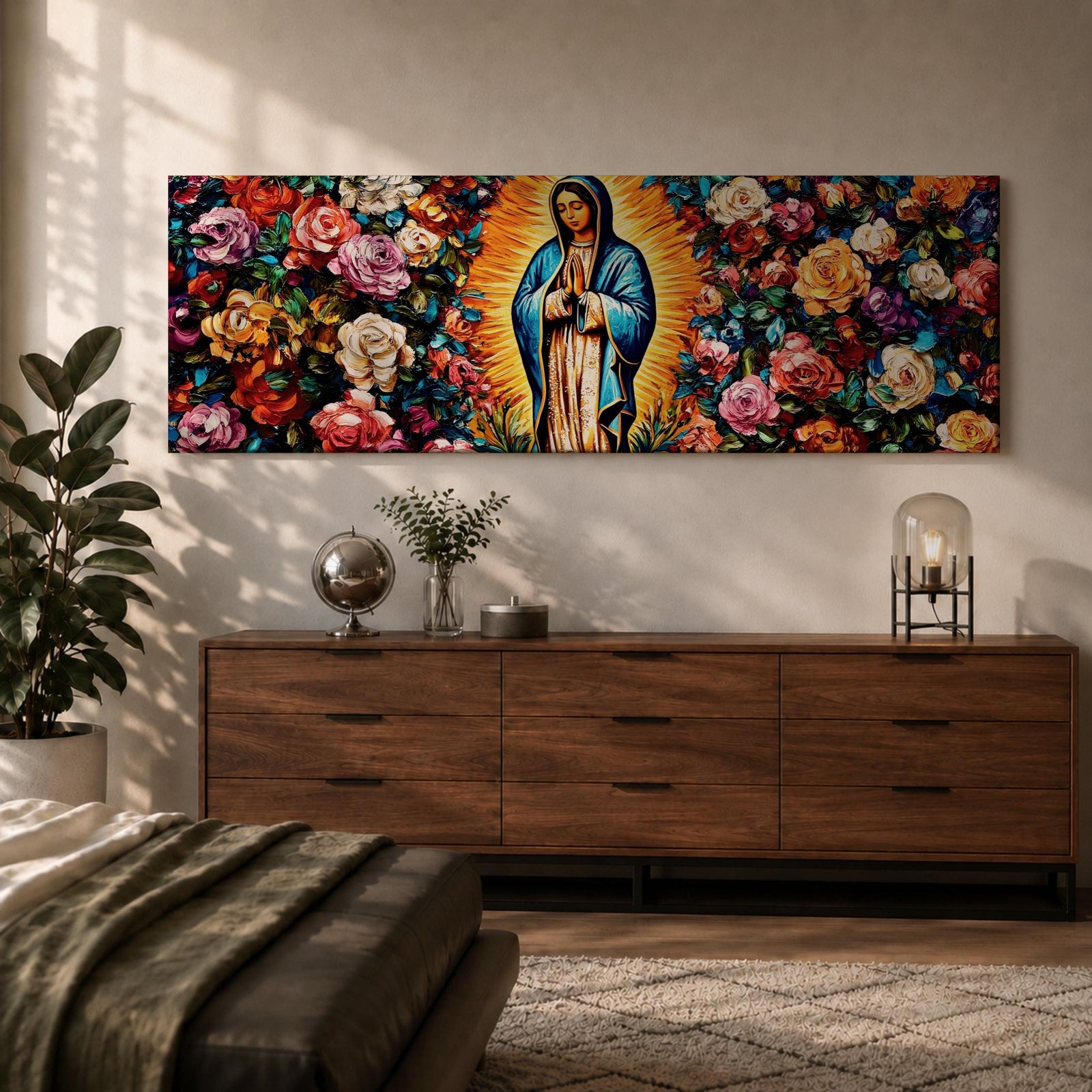 A long panoramic painting of Mary of Guadalupe standing in prayer with hands folded and head bowed, surrounded by radiant golden rays. She wears a blue mantle over a rose colored gown while vibrant roses and colorful flowers fill the background, creating a devotional Catholic Marian image across a wide horizontal composition.