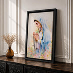 A watercolor style framed canvas depicting Virgin Mary in profile, wearing a blue and white veil with gold trim, holding a rosary and praying, surrounded by soft floral colors and a gentle light background.